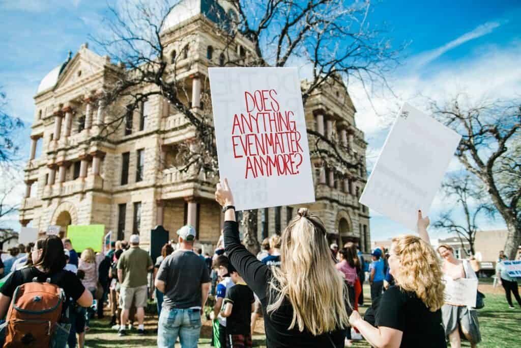 woman holding does anything even matter anymore? signage near building at daytime